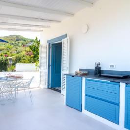 Bright kitchen with blue cabinets, white table set, and mountain view from open doors.