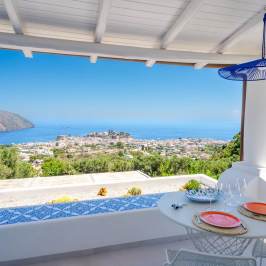 Covered patio with sea view, round table, chairs, and decorative plates under a blue lantern.