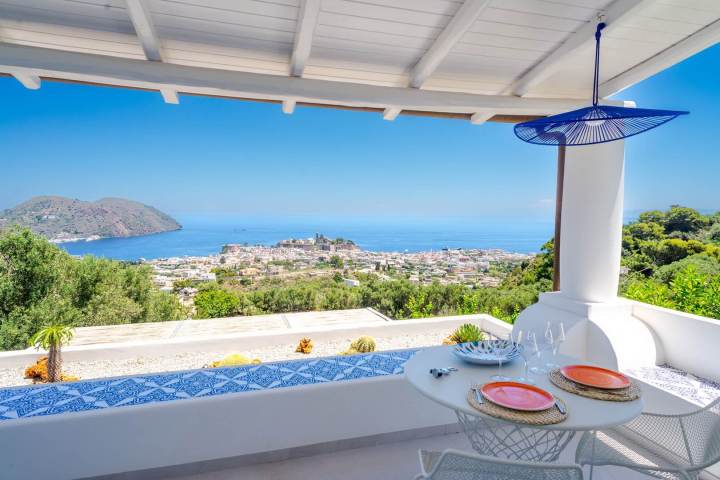 Covered patio with sea view, round table, chairs, and decorative plates under a blue lantern.