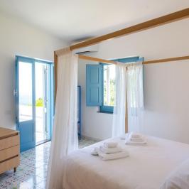 Bright bedroom with a canopy bed, blue shutters, and wooden dresser.