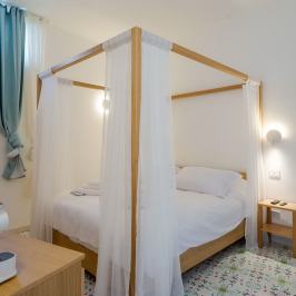 Cozy bedroom with a canopy bed, sheer curtains, small nightstand, and light blue curtains.