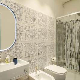 Bathroom with abstract wall tiles, oval mirror, and glass shower enclosure.