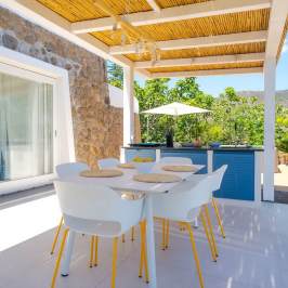 Outdoor patio with white table and chairs, wooden pergola, plants, and mountain view.