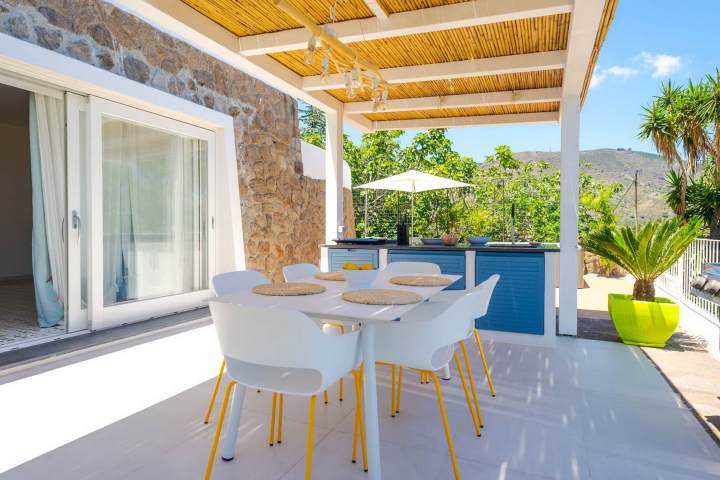 Outdoor patio with white table and chairs, wooden pergola, plants, and mountain view.