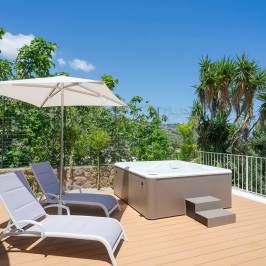 Deck with two loungers, umbrella, and hot tub overlooking trees and landscape under a clear sky.