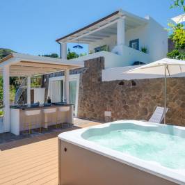 Outdoor patio with a hot tub, bar, and lounge chairs under a sunny sky.