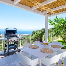 Outdoor patio with grill, dining table, and ocean view under a pergola.