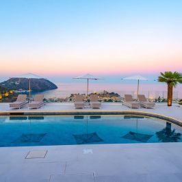 Infinity pool with loungers, umbrellas, and ocean sunset view.