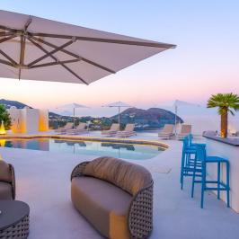 Luxurious poolside lounge area with sea view, umbrellas, and seating under a clear twilight sky.