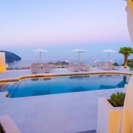 Luxury pool with lounge chairs and umbrellas overlooking ocean at sunset.
