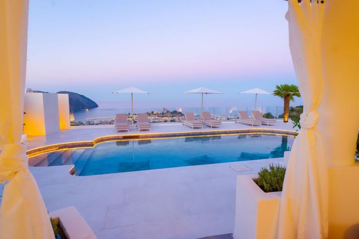 Luxury pool with lounge chairs and umbrellas overlooking ocean at sunset.