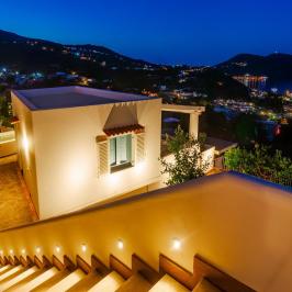 Evening view of a house and city lights near a bay under a blue sky.
