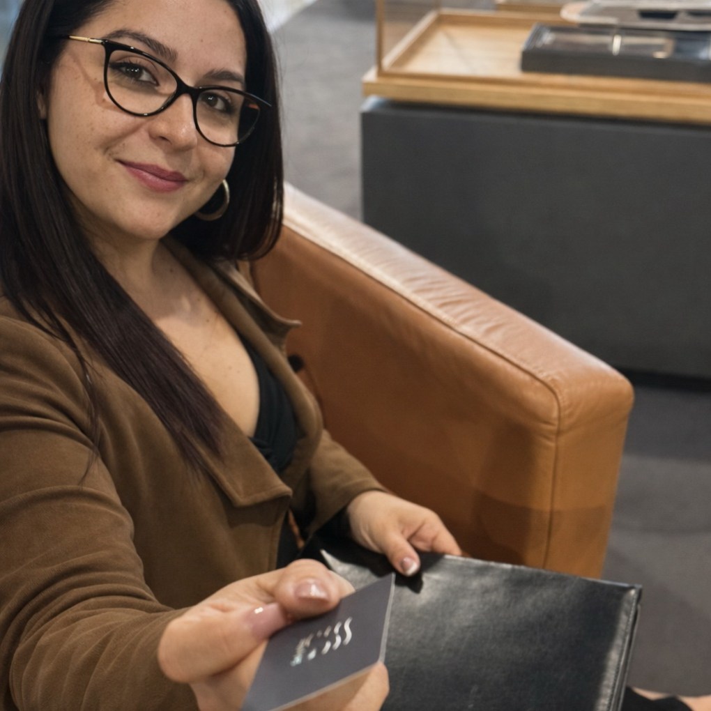 Woman in glasses sitting on couch, smiling and handing a card.