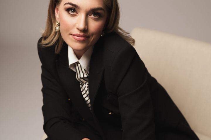 Woman in black suit sitting on chair, looking confidently forward.