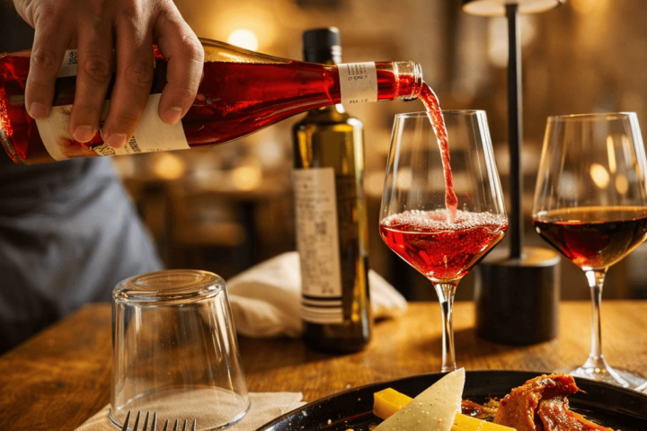 Red wine poured into glass beside plate of appetizers in cozy restaurant.