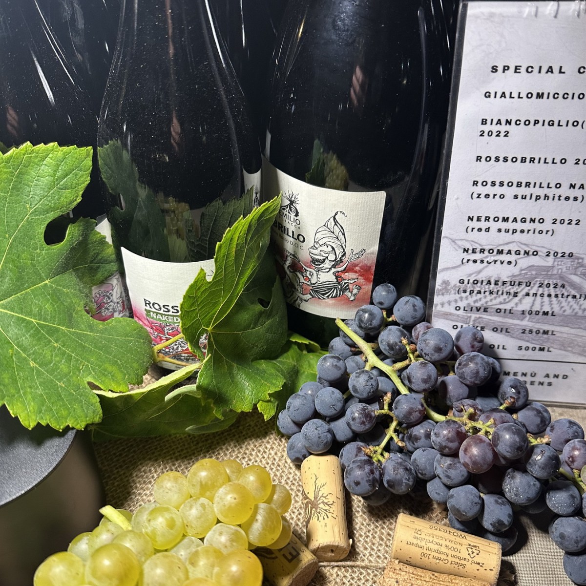 Wine bottles with grapes and corks beside a menu on a burlap surface.