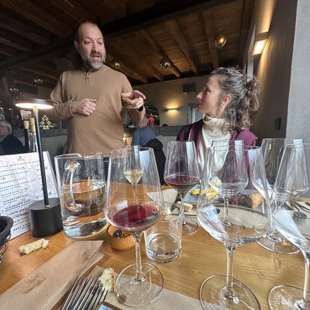 Man talking to woman at a table with multiple wine glasses.