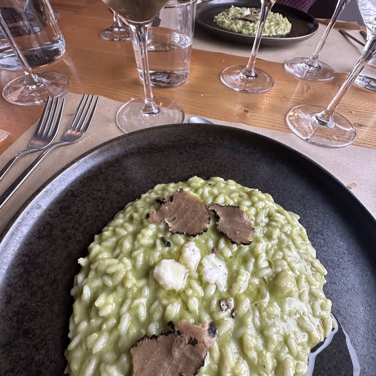 Plate of risotto with truffles, surrounded by glasses of white wine on a wooden table.