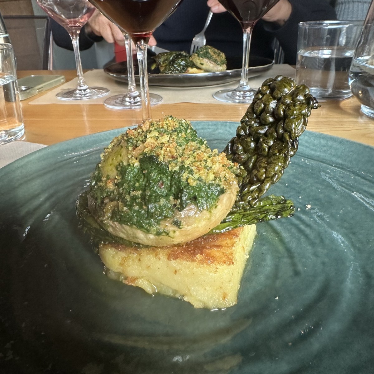 Gourmet dish with wine glasses in the background.
