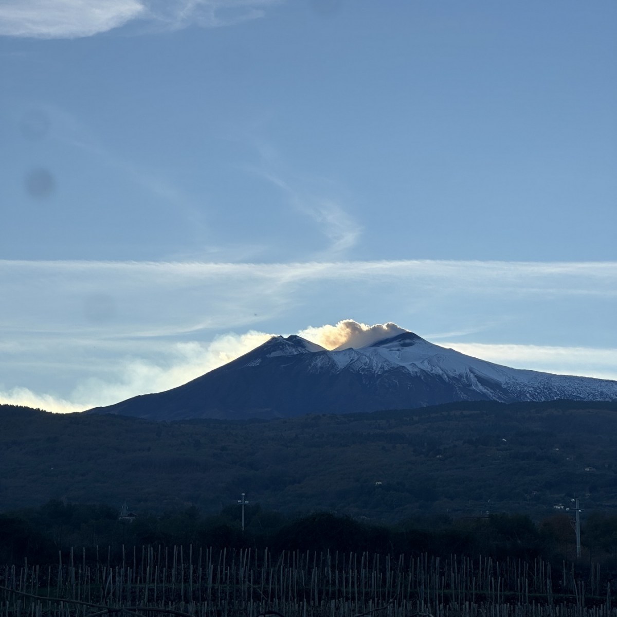 Mountain with snow peak under blue sky, smoke rising.