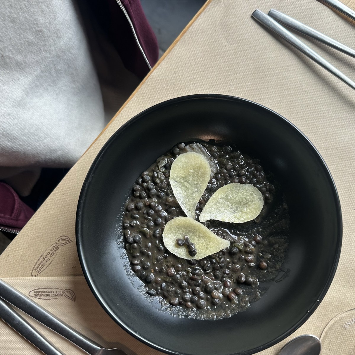Black bowl with lentils and decorative potato slices on a table.