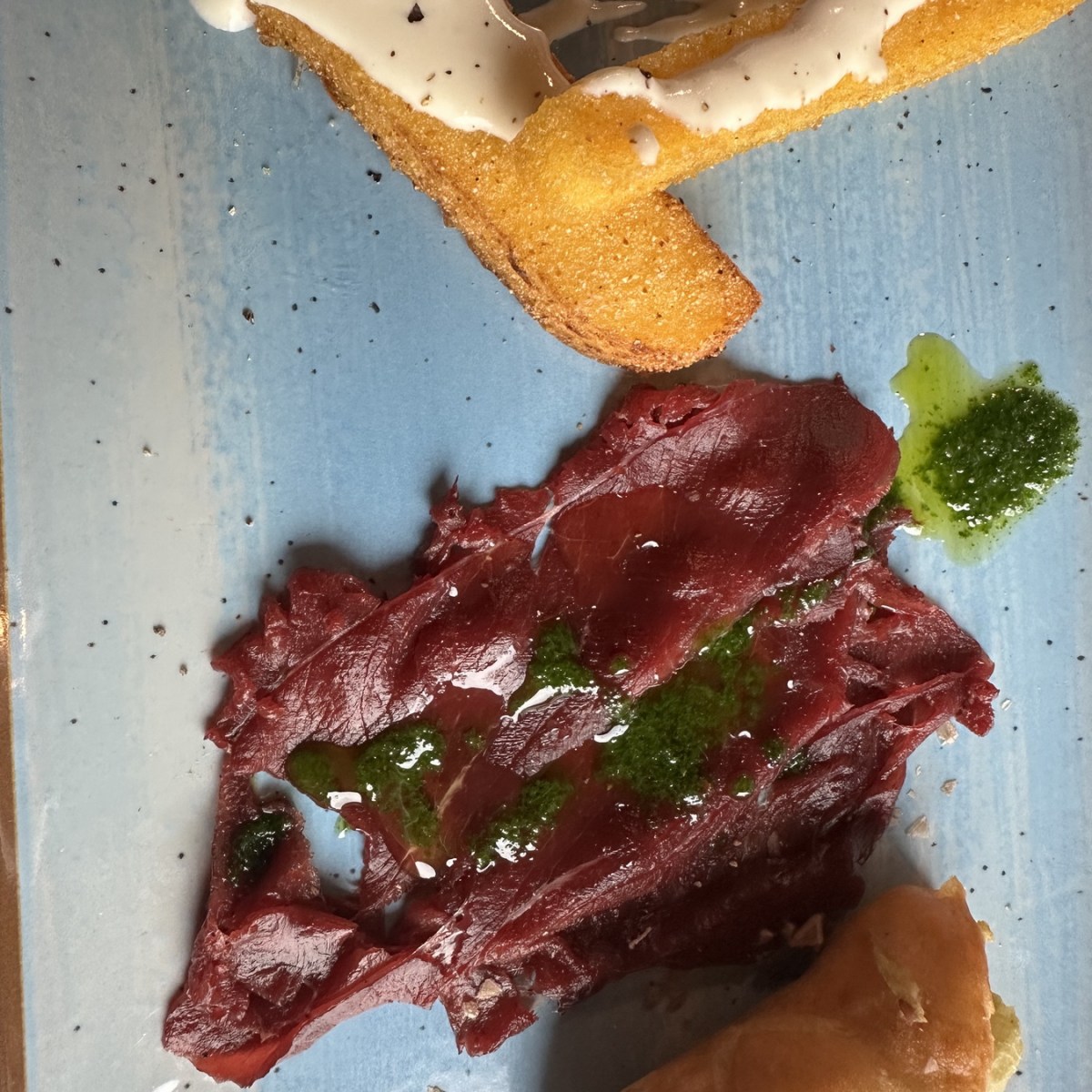 Plate with beetroot carpaccio, breadstick, sauce, and a small serving of stuffed pastry.