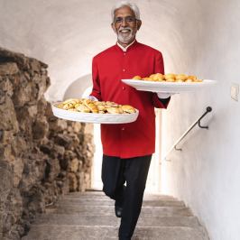 Man in red uniform walking up steps carrying trays of pastries.