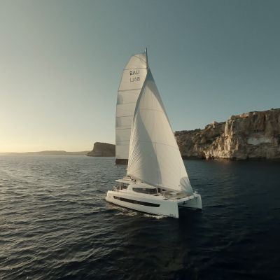 Sailboat on calm sea near rocky cliffs under a clear sky.
