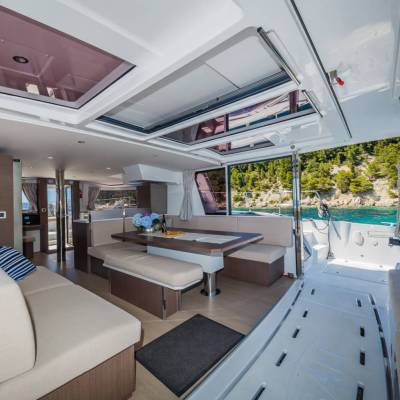 Interior of a modern yacht with sofas, table, and open deck, surrounded by water and trees.