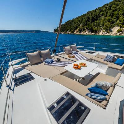 Luxury yacht deck with sun loungers, pillows, and snacks, overlooking blue sea and forested coastline.