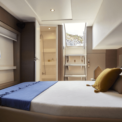 Modern boat cabin with bed, pillows, window, and stairs to door.