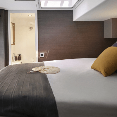 Camper bed with gray and mustard pillows, blanket, and view into white bathroom.