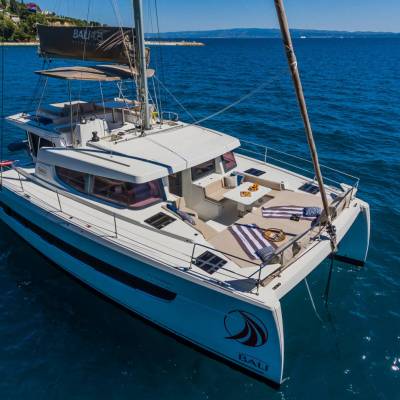 White catamaran sailing on calm blue sea under clear sky.