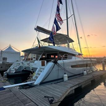 Sailboat docked at sunset, flags on mast, calm water.