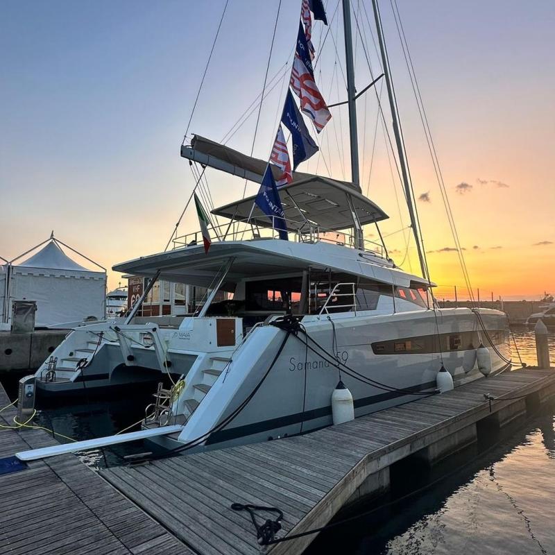 Sailboat docked at sunset, flags on mast, calm water.