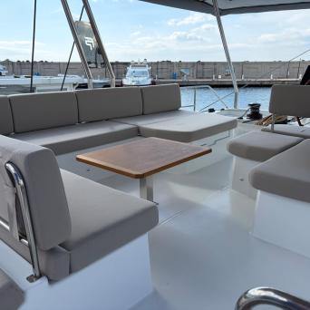 Yacht deck with cushioned seating around a table, water and other boats in background.