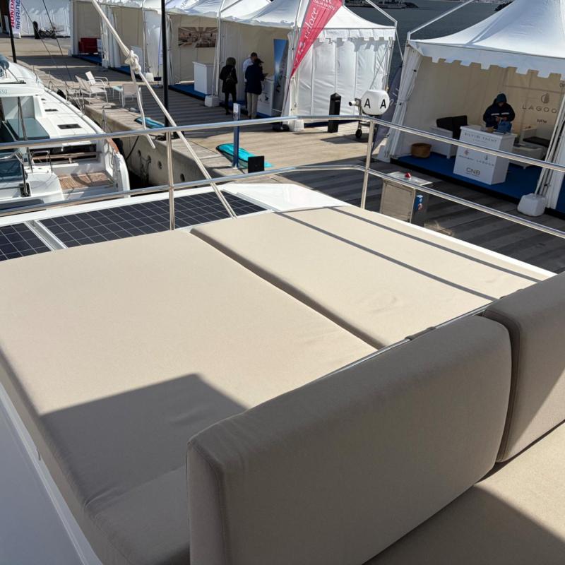 Sunbed on yacht deck with tents and people in background.