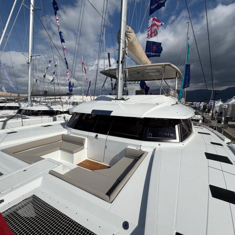 Catamaran yacht docked at marina with flags and seating area on deck