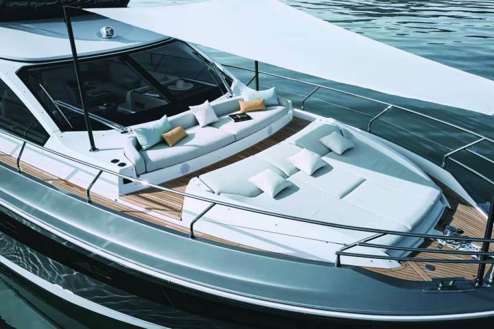 Luxury yacht deck with lounge chairs, cushions, and sunshade on calm water.