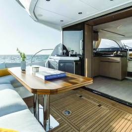 Elegant yacht with outdoor seating, wooden table, and open sliding doors to cabin, overlooking the sea.