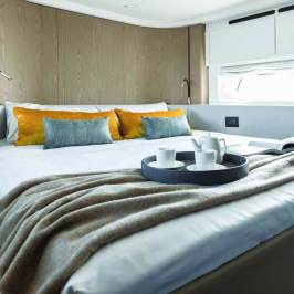 Modern bedroom with bed, orange pillows, tray with cups, and window.