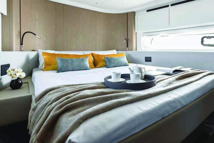 Modern bedroom with bed, orange pillows, tray with cups, and window.