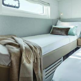 Cozy cabin with twin beds, pillows, and a blanket beside a small nightstand.