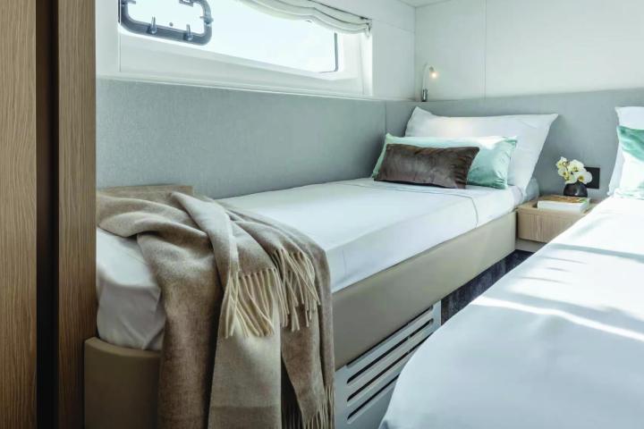 Cozy cabin with twin beds, pillows, and a blanket beside a small nightstand.