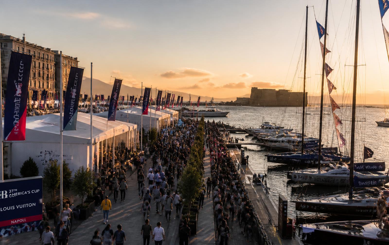 Crowd at a coastal event with boats docked at sunset.